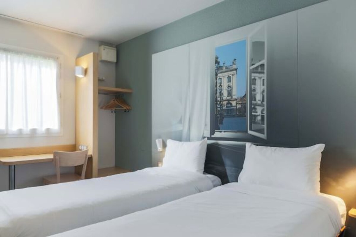 A hotel room with two beds, a desk, and a large window with a cityscape view.
