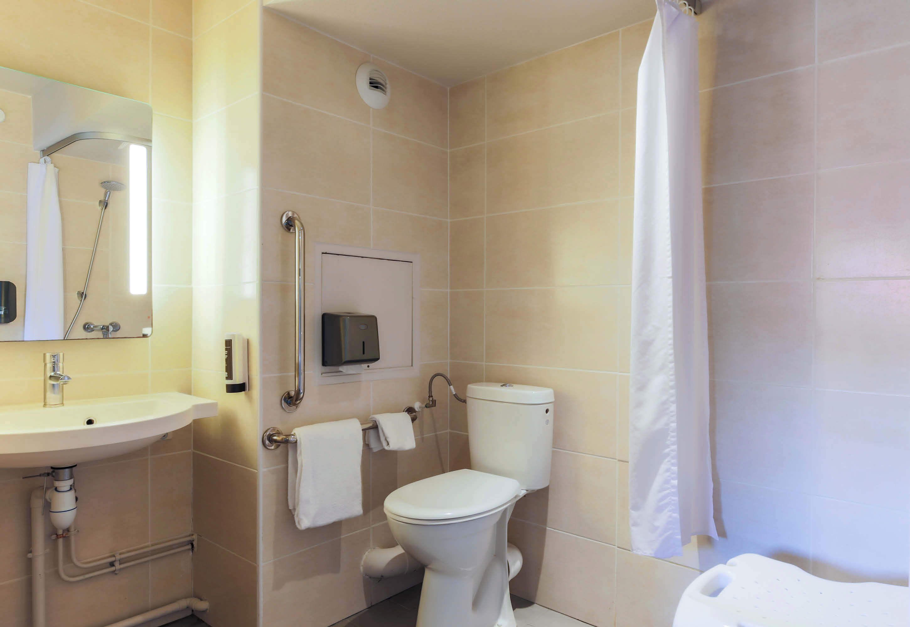 A bathroom with a toilet, sink, shower, and a hand sanitizer dispenser.