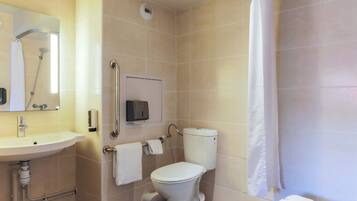 A bathroom with a toilet, sink, shower, and a hand sanitizer dispenser.