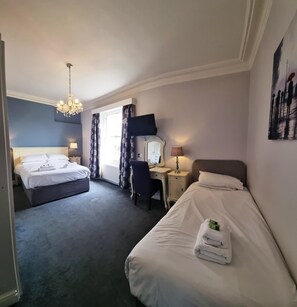 A hotel room with two beds, a desk, a chair, a television, and a chandelier.