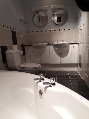 A modern bathroom with a bathtub, two sinks, a toilet, and a mirror above the sinks. - Anglesey Hotel (Gosport)