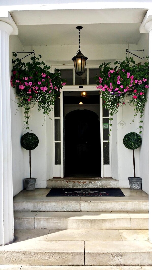 A front entrance with a black door, a white porch, and two potted plants on either side.