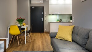 Un espace de vie compact comprenant un coin repas, une kitchenette et un canapé gris agrémenté d’un coussin à motifs.
