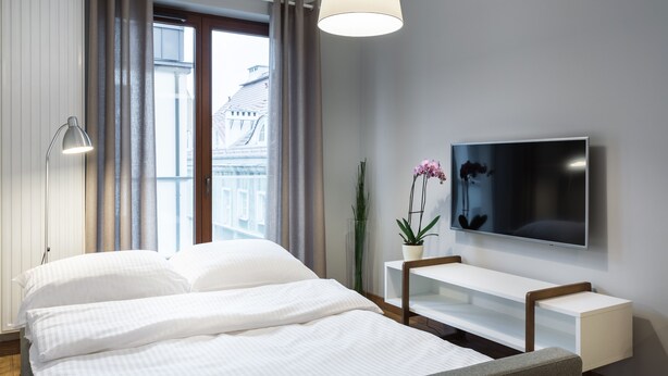 Une chambre d’hôtel moderne avec un grand lit, un téléviseur fixé au mur, une table de chevet et une fenêtre avec des rideaux.