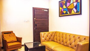 A living room with a brown leather sofa, a brown leather armchair, and a glass coffee table. - Hotel Quo Vadis (Abuja)