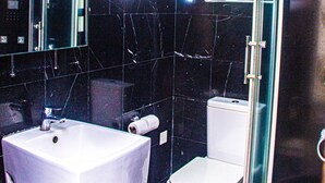 A bathroom with a white sink, a toilet, and a glass-enclosed shower. - Hotel Quo Vadis (Abuja)