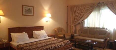 A hotel room with a bed, two chairs, a sofa, a small table, and an air conditioning unit.
