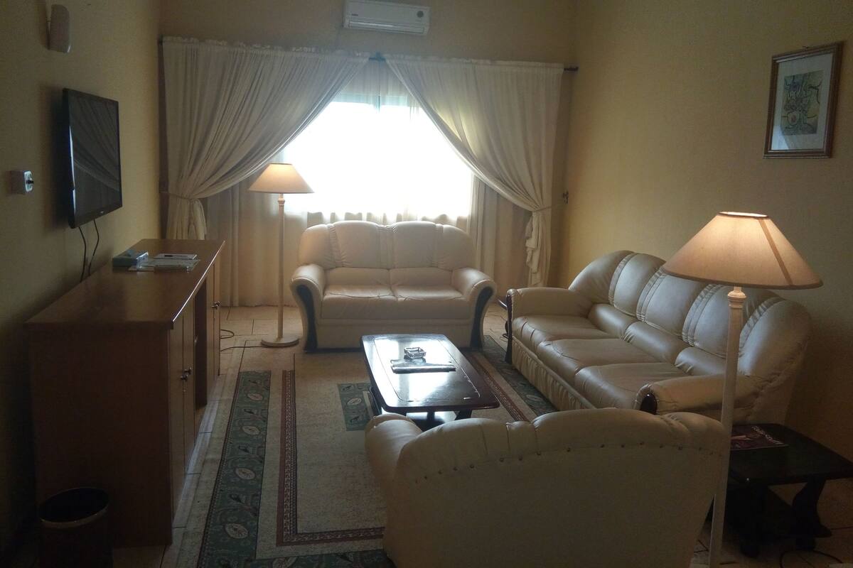 A living room with a sofa, two armchairs, a coffee table, a TV, and a lamp.