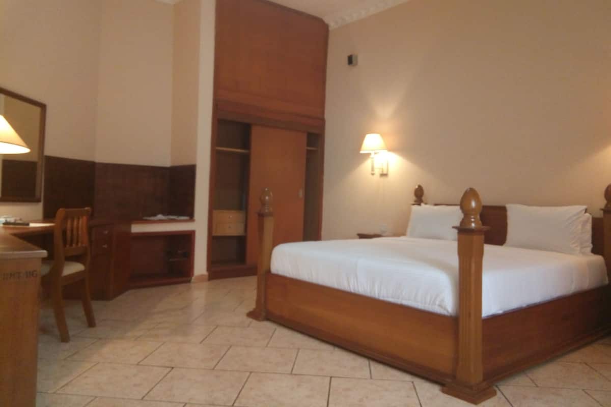 A hotel room with a bed, desk, chair, and wardrobe.