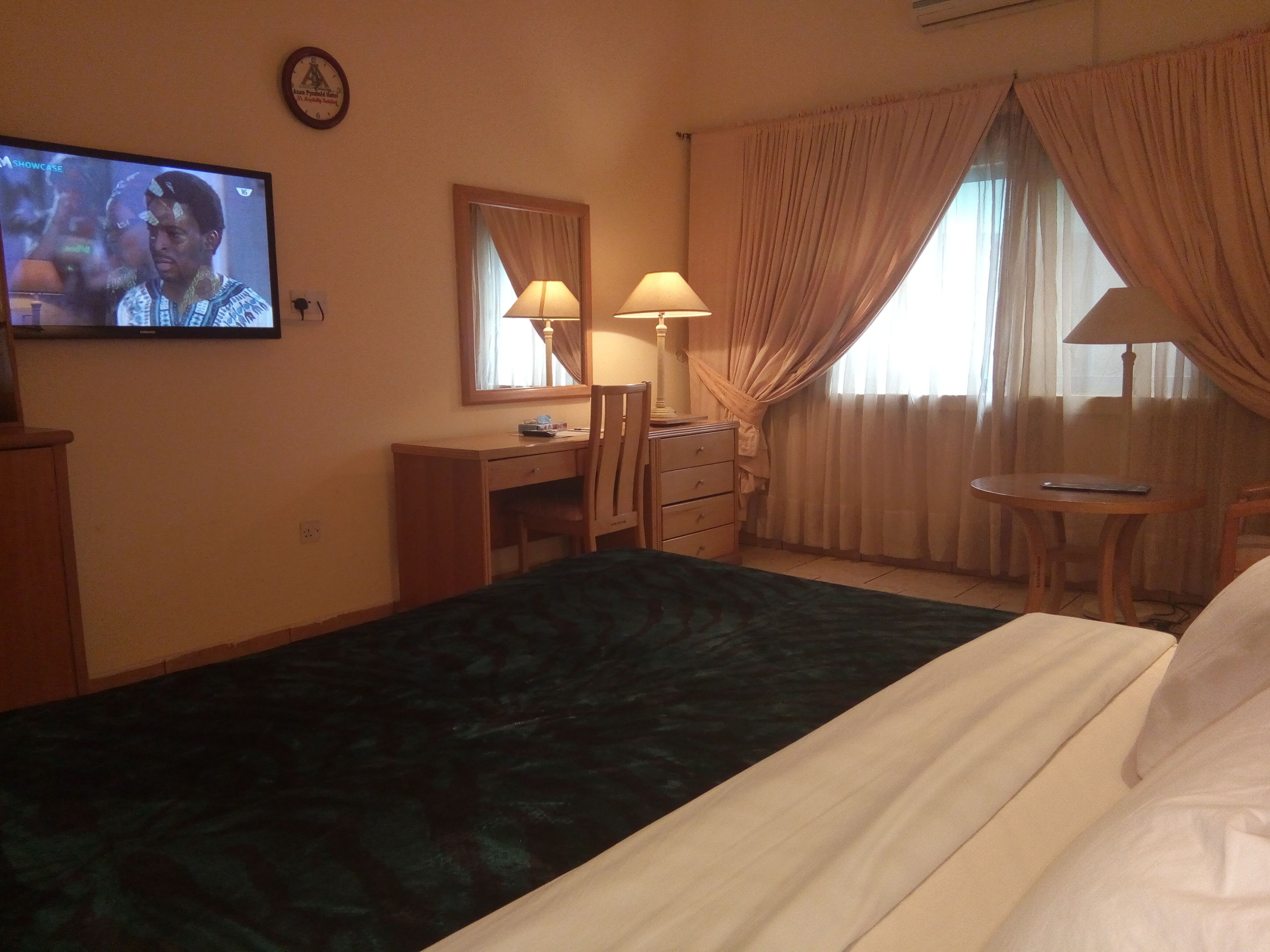 Een hotelkamer met een bed, bureau, stoel, televisie en raam met gordijnen.