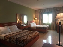 Habitación de hotel con dos camas, un escritorio, una silla, una lámpara y una ventana con cortinas.