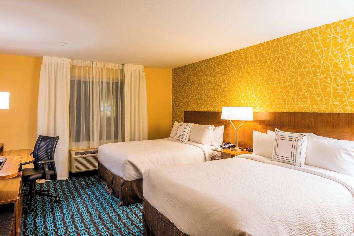 Une chambre d’hôtel avec deux lits, un bureau, une chaise et une fenêtre avec des rideaux.