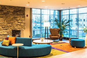 A modern lobby with a stone wall, a blue sofa, a round table, and a large window with a view of the street. - Fairfield Inn & Suites by Marriott Atlanta Fairburn (Fairburn)