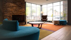 A modern lounge area with a stone fireplace, comfortable seating, and large windows offering a view of the outdoors. - Fairfield Inn & Suites by Marriott Atlanta Fairburn (Fairburn)