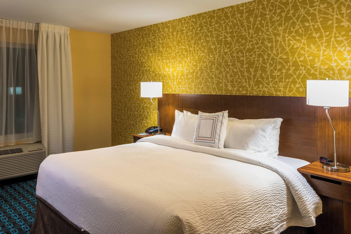 Une chambre d’hôtel avec un grand lit, deux lampes de chevet, une tête de lit en bois et un papier peint à motifs.