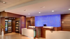 A hotel reception area with a counter, a refrigerator stocked with beverages, and a blue-lit wall. - Fairfield Inn & Suites by Marriott Atlanta Fairburn (Fairburn)