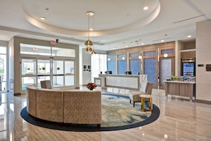 Eine moderne Lobby mit einer Rezeption, einer Sitzecke mit rundem Tisch und einem großen Fenster mit Blick nach draußen.