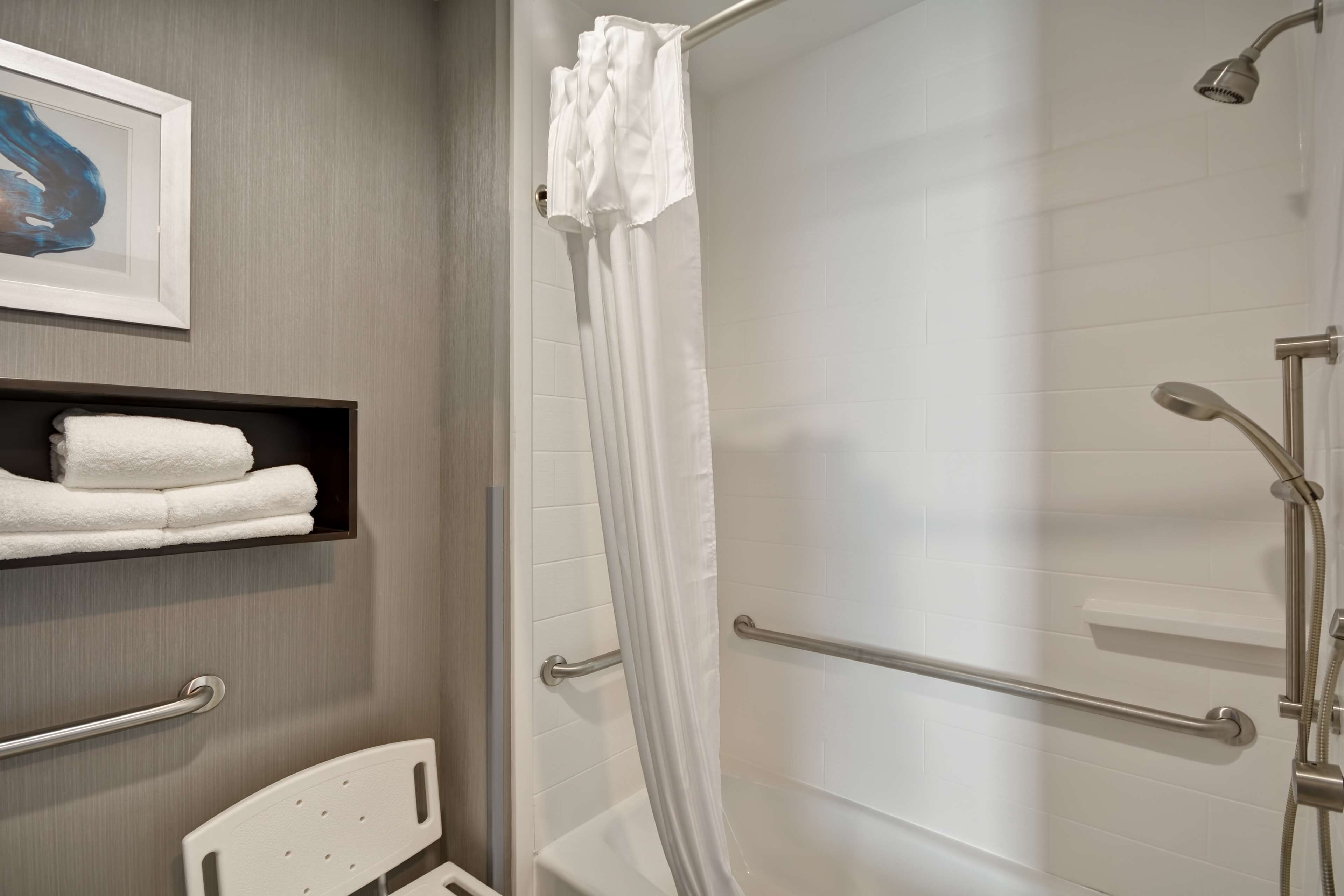 A modern bathroom with a shower, a white towel rack, and a framed artwork on the wall.