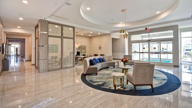 A spacious lobby with a curved ceiling, a seating area with a sofa and chairs, a decorative wall, and a large window providing a view outside. - Homewood Suites by Hilton Conroe (Conroe)
