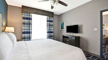A hotel room with a large bed, a ceiling fan, a flat-screen TV, and a window with curtains.