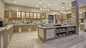 A modern kitchen with wooden cabinets, a central island with a sink, and a buffet area with plates and glasses. - Homewood Suites by Hilton Conroe (Conroe)