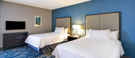 A hotel room with two beds, a ceiling fan, a flat-screen TV, a desk with drawers, a lamp, and a framed picture on the wall.