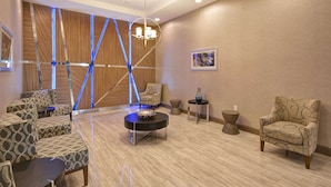 A modern lounge area with patterned sofas, a central coffee table, and a unique ceiling design with blue lighting accents. - Homewood Suites by Hilton Conroe (Conroe)