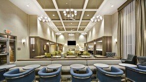 A hotel lobby with a central seating area, multiple tables, and a chandelier. - Homewood Suites by Hilton Detroit (Warren)
