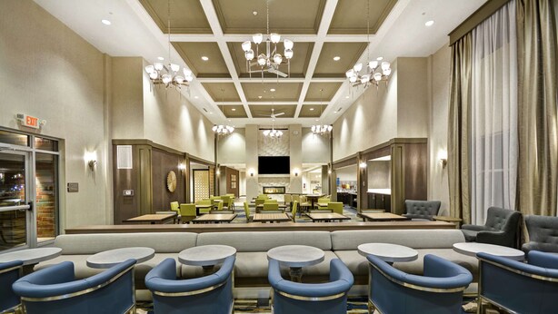 A hotel lobby with a central seating area, multiple tables, and a chandelier. - Homewood Suites by Hilton Detroit (Warren)