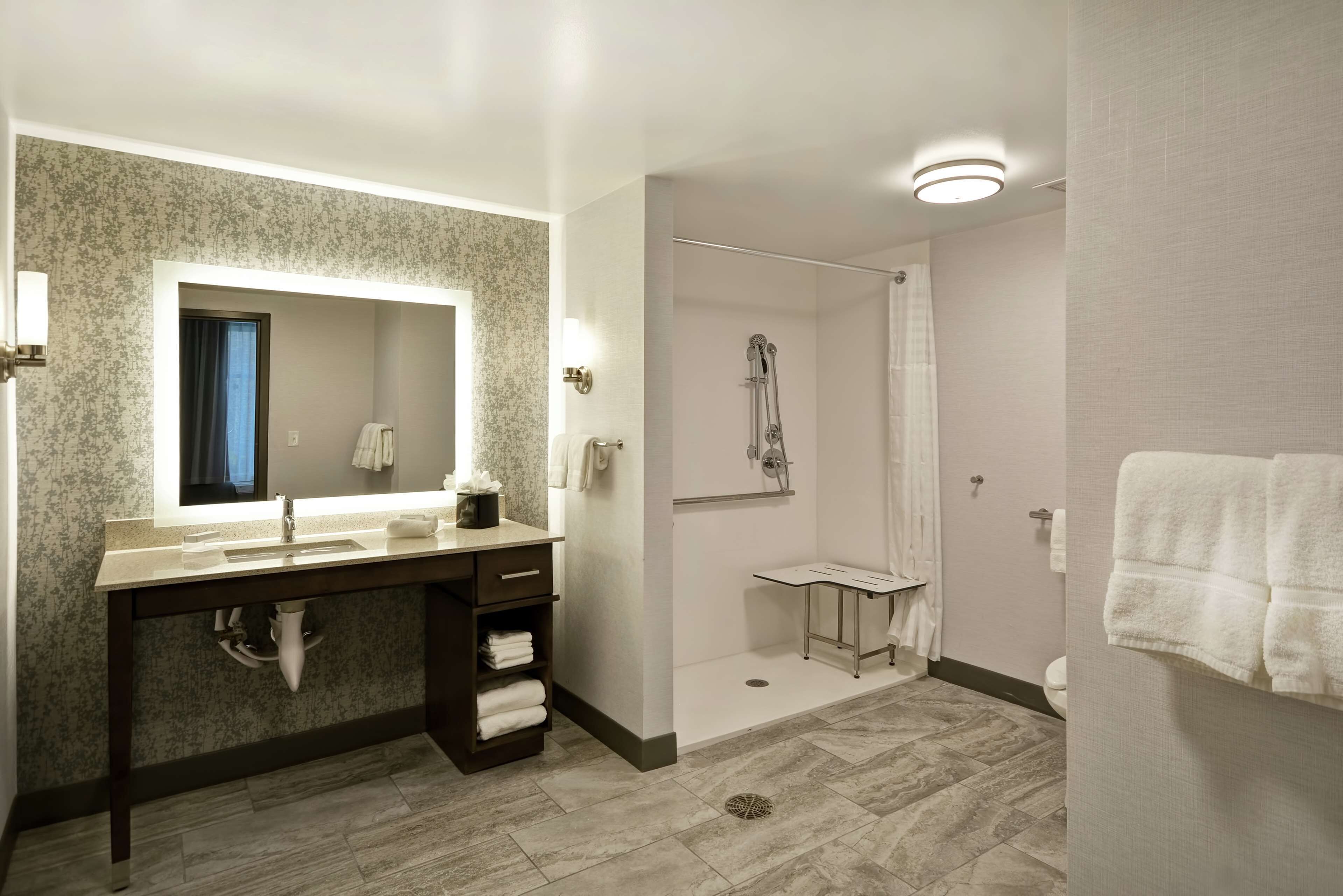 A modern bathroom with a large mirror, a sink, a shower, and a toilet.