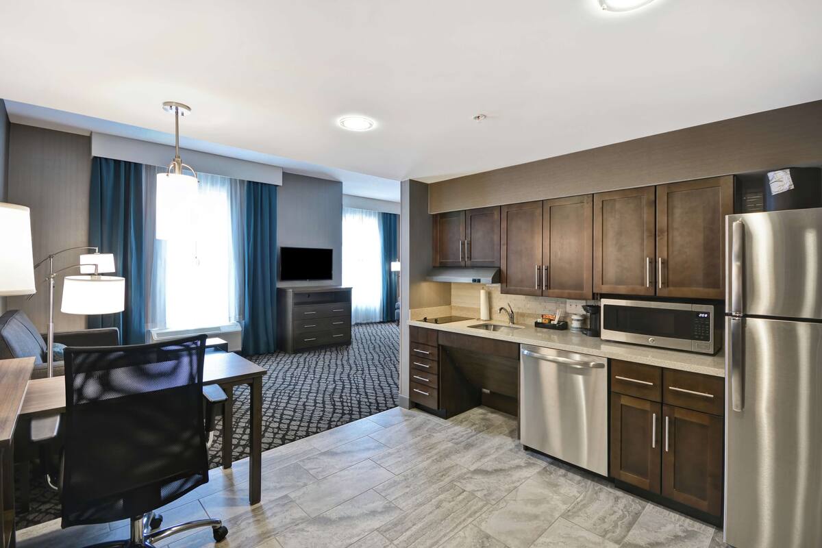 A modern hotel room with a kitchenette, a dining area, and a TV.