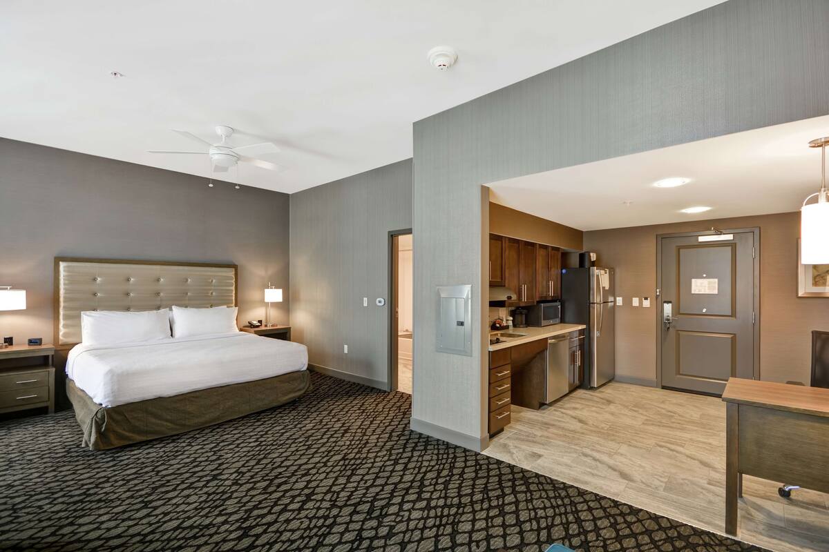 A hotel room with a large bed, a desk, and a kitchenette.