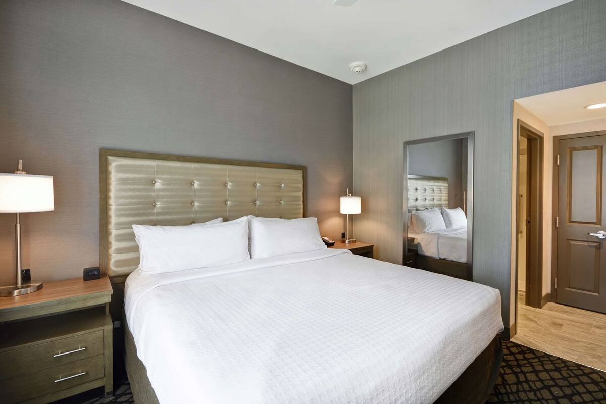 A hotel room with a large bed, bedside tables, a mirror, and a door.
