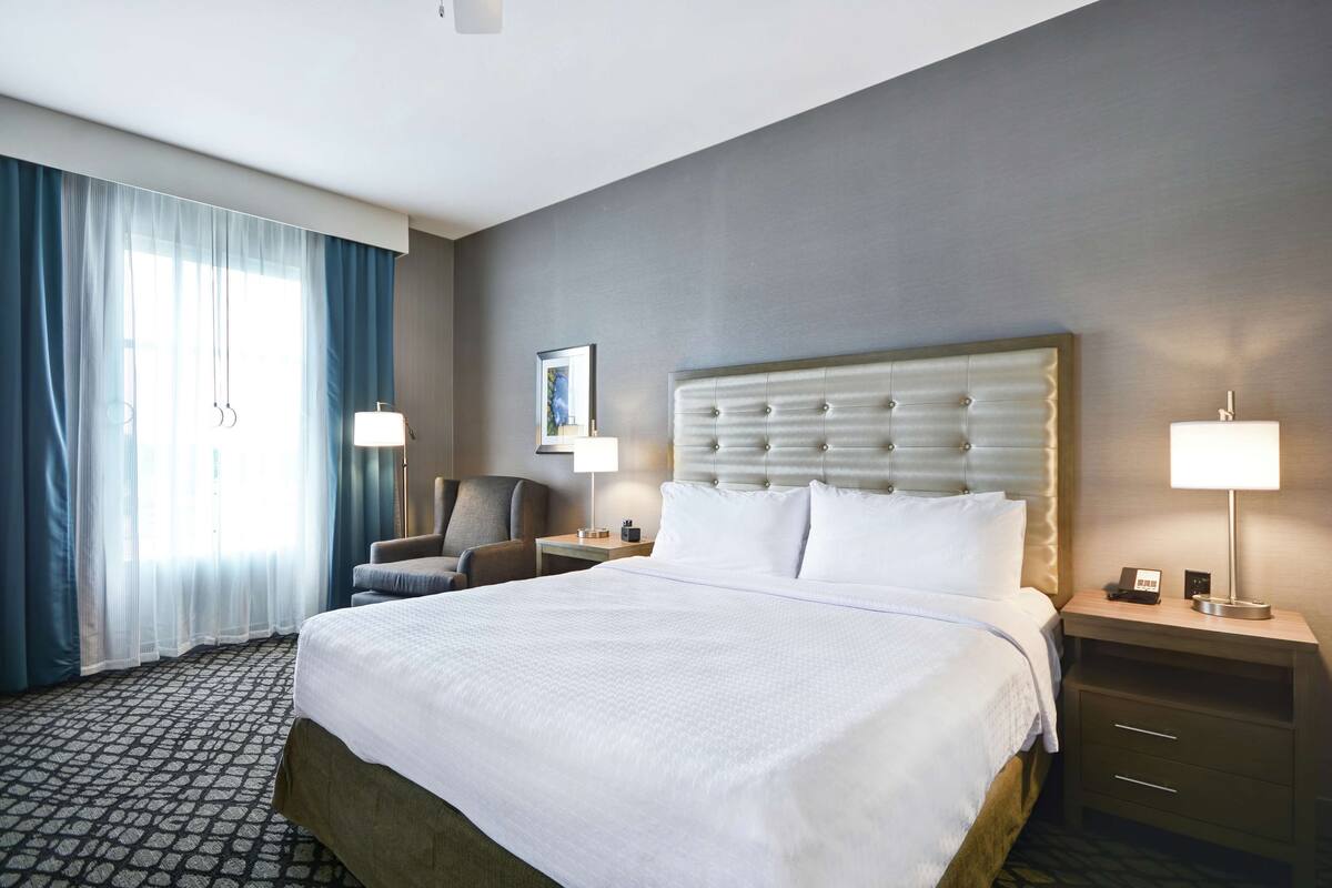 A hotel room with a large bed, a chair, a desk, and a lamp.