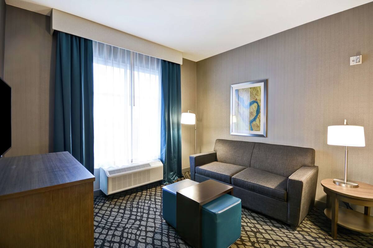 A hotel room with a sofa, a small table, a TV, and a window with curtains.