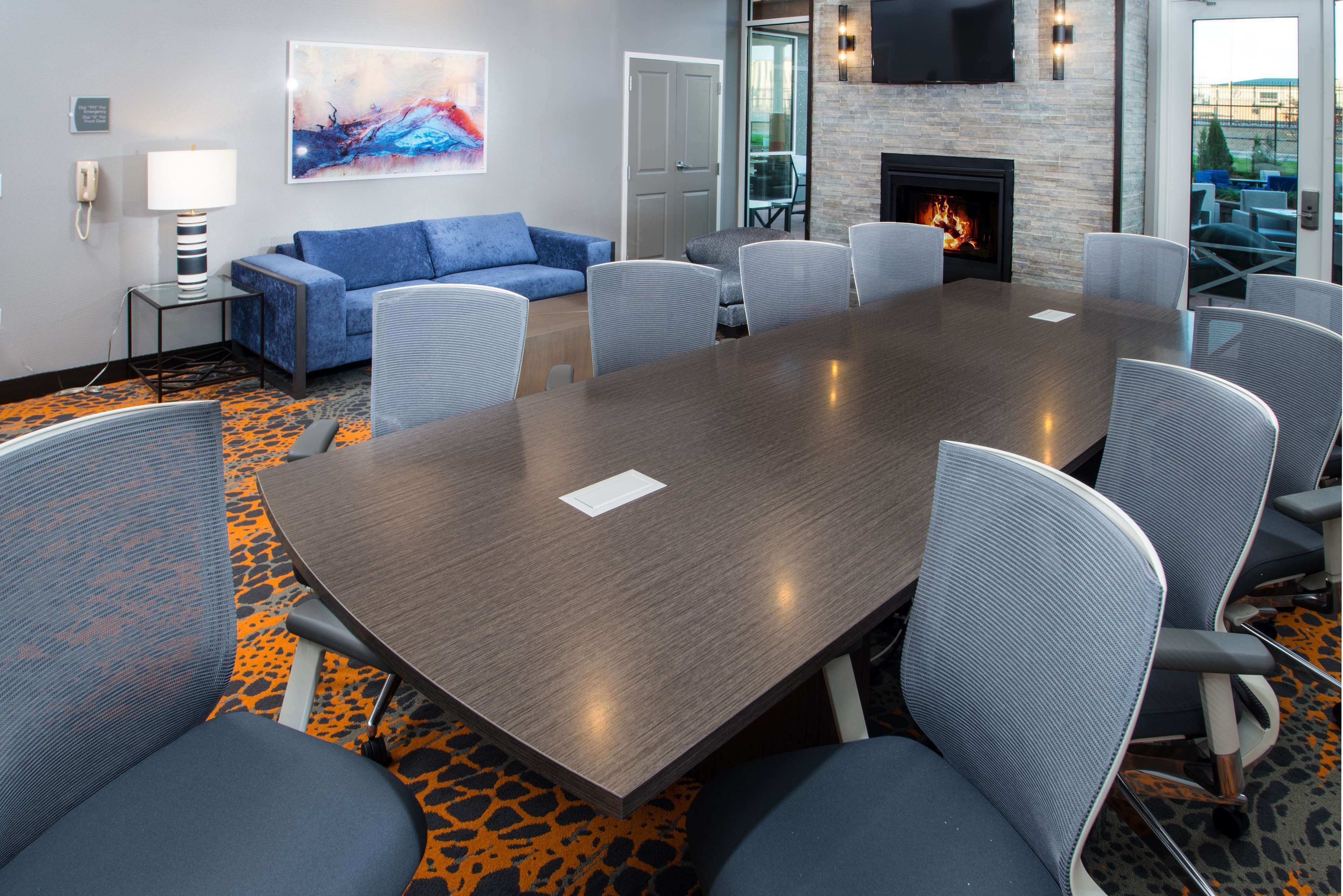 A conference room with a large table, chairs, a sofa, a fireplace, and a TV on the wall.