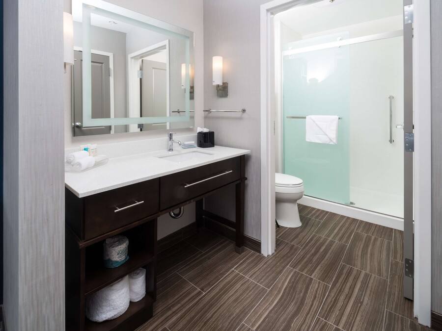 A modern bathroom with a white sink, dark wood vanity, a glass shower enclosure, and a white toilet.