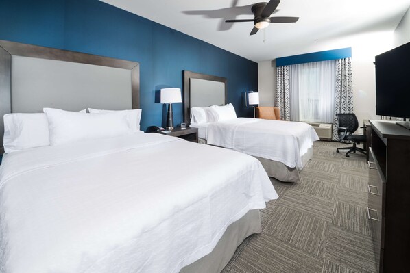 A hotel room with two beds, a desk, a chair, a television, and a ceiling fan.
