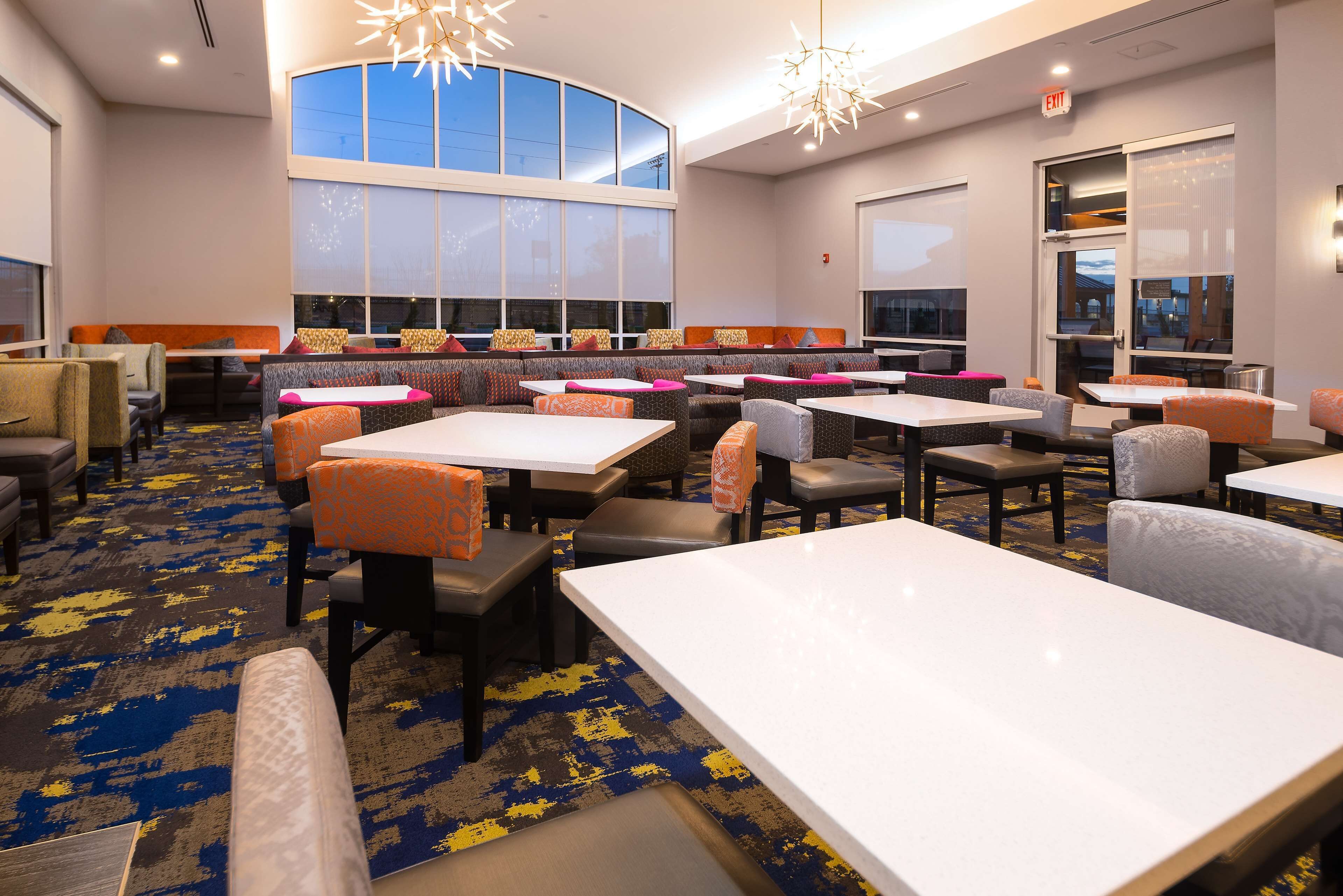 A hotel lobby with multiple seating areas, including booths and tables, and large windows providing natural light.