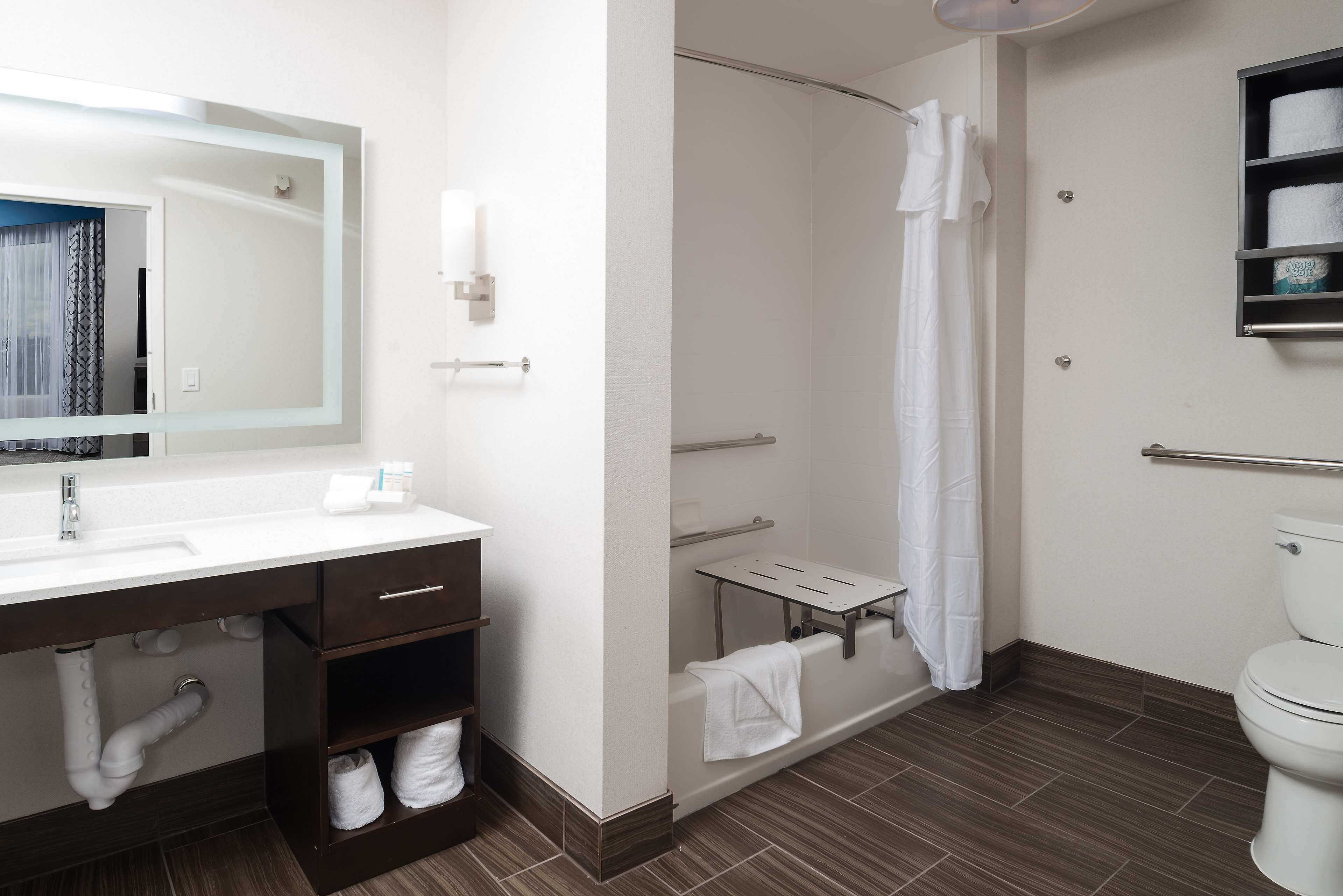 A modern bathroom with a white sink, vanity, and toilet. It includes a shower area with a glass door and a towel rack.