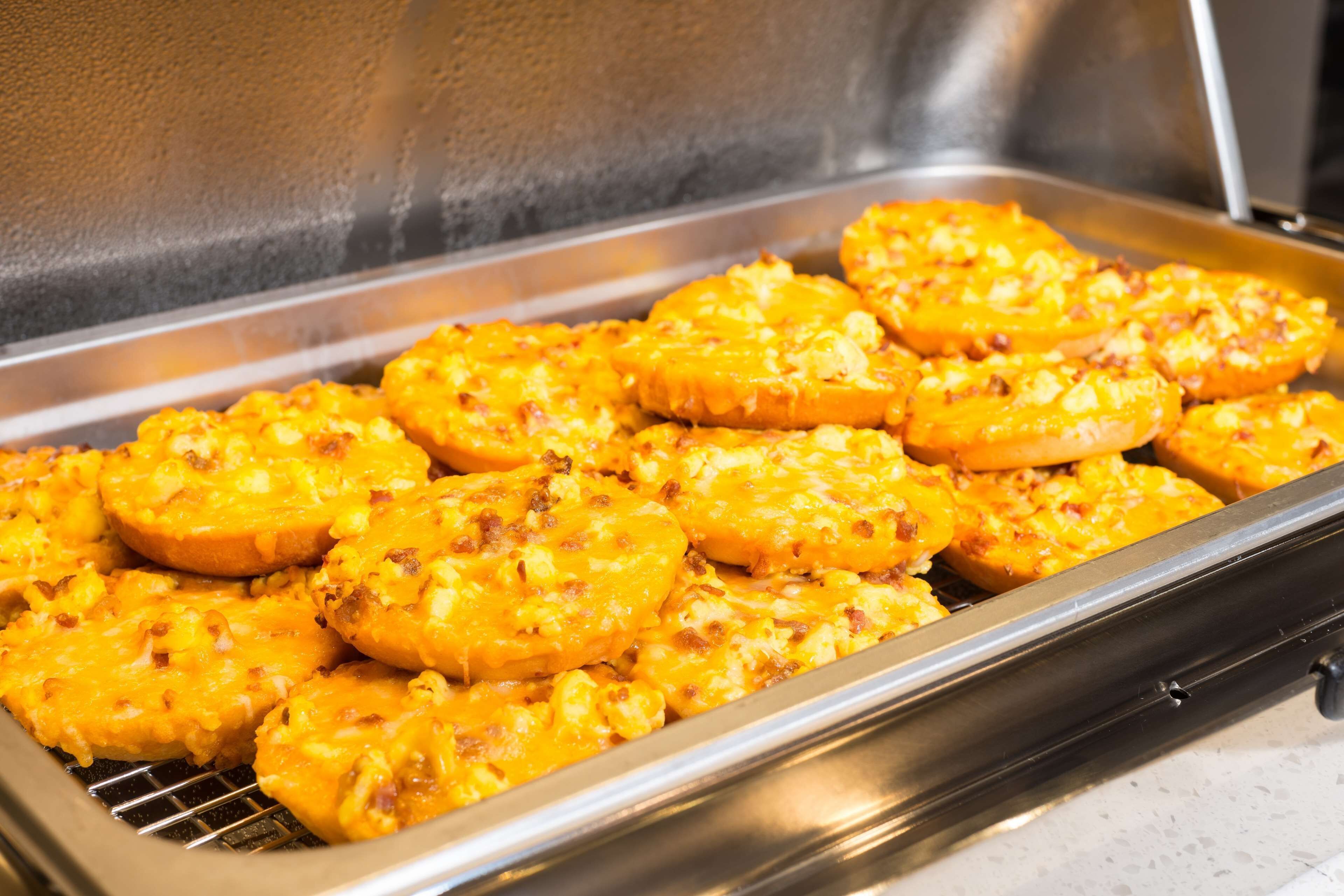 A buffet tray with baked potato wedges topped with melted cheese and bacon.
