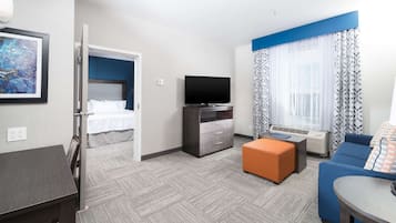 A hotel room with a bed, a TV, a desk, a sofa, and a window with curtains.