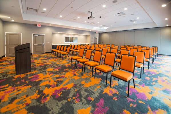 Un salón de conferencias con filas de sillas anaranjadas, un atril y suelo alfombrado.