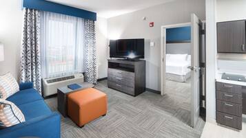 Habitación de hotel con sofá, reposapiés, televisión, escritorio y kitchenette.
