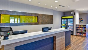Un área de recepción moderna de hotel con un quiosco digital, un letrero 'HOME 21' y un letrero de 'Hilton Honors'.