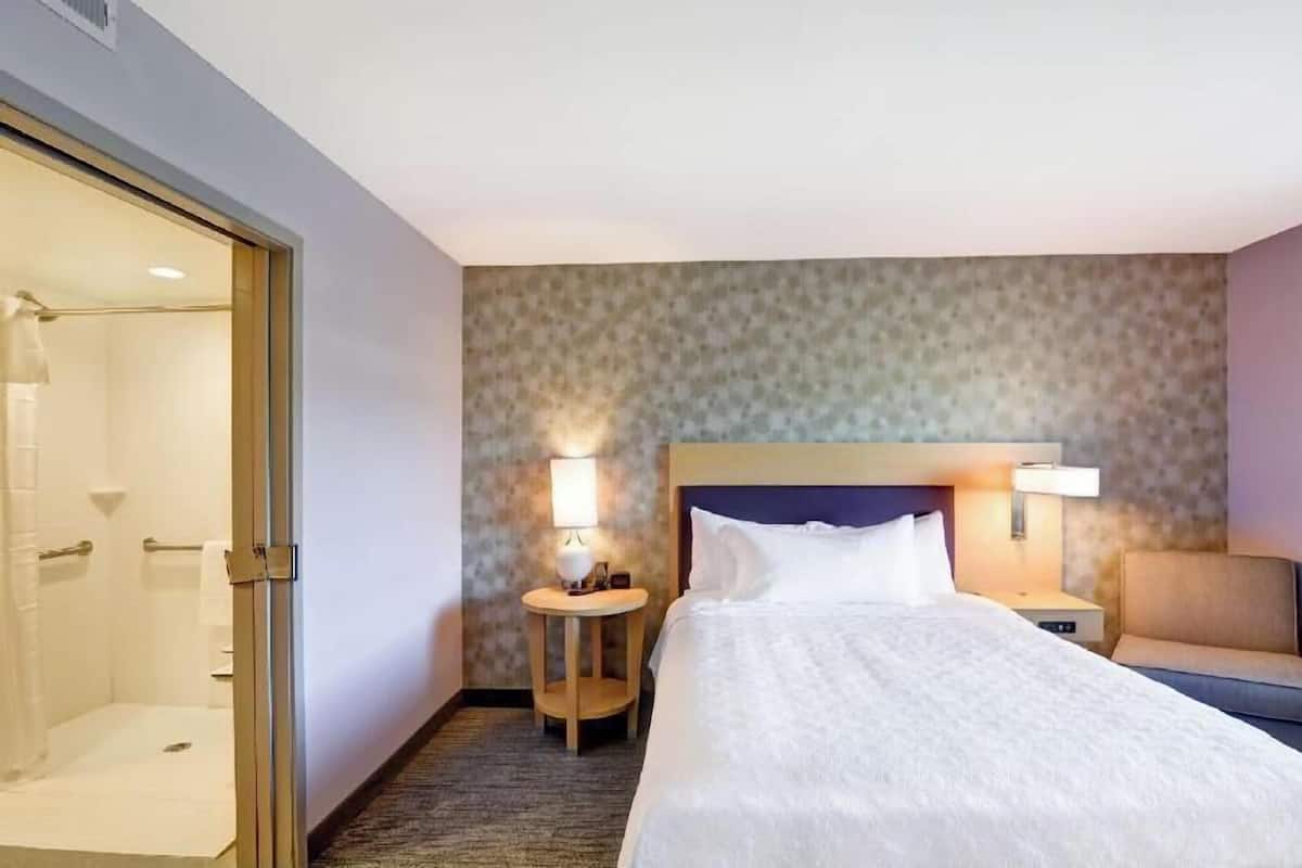 A hotel room with a bed, bedside lamps, a round table, and a shower area.
