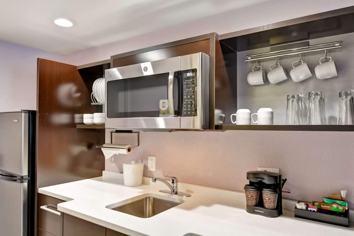 A modern kitchen with a stainless steel microwave, a coffee maker, and a set of mugs on the wall.