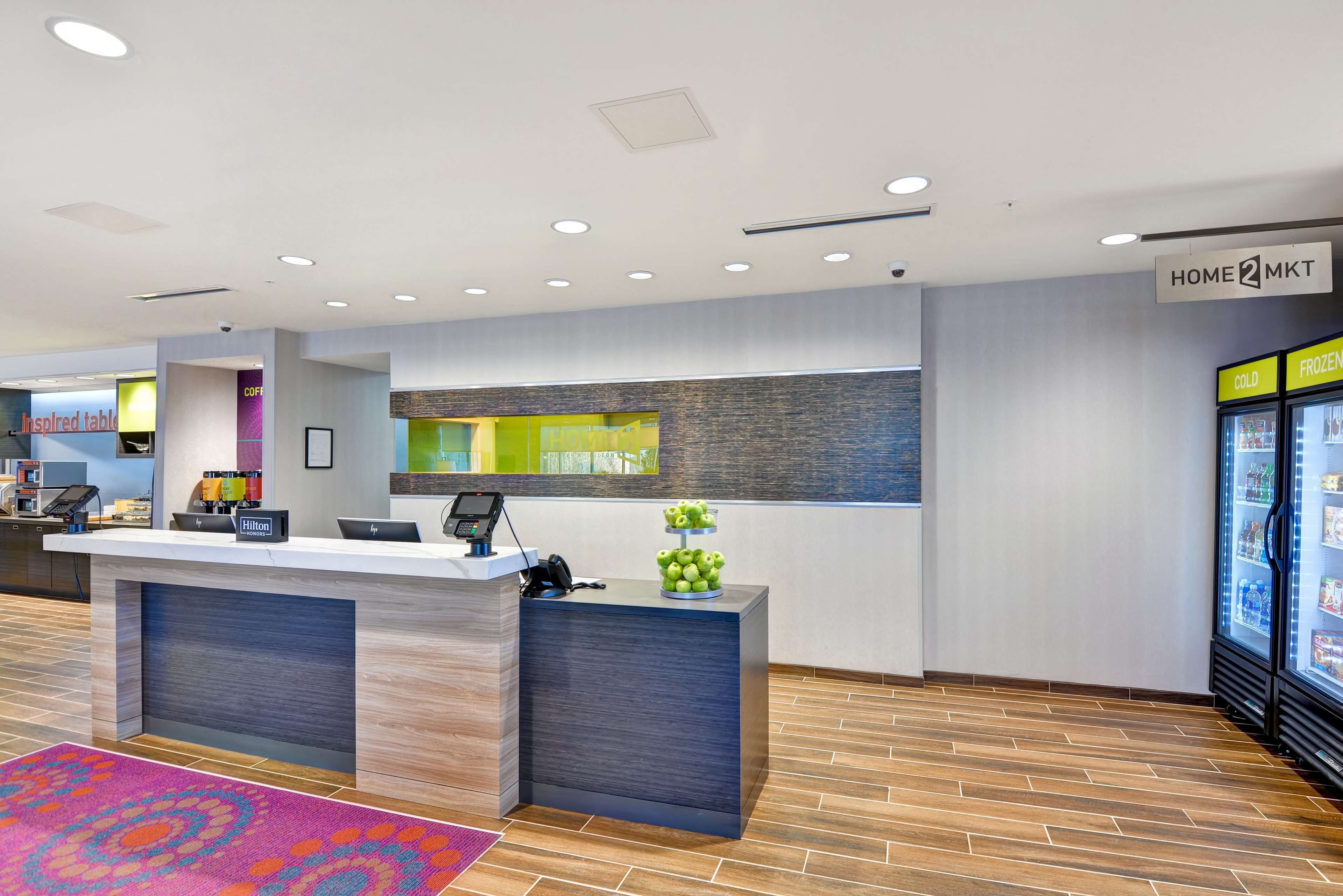 Un'area reception di un hotel dal design moderno, con una scrivania reception, un display digitale e un frigorifero con vani per prodotti freddi e surgelati.