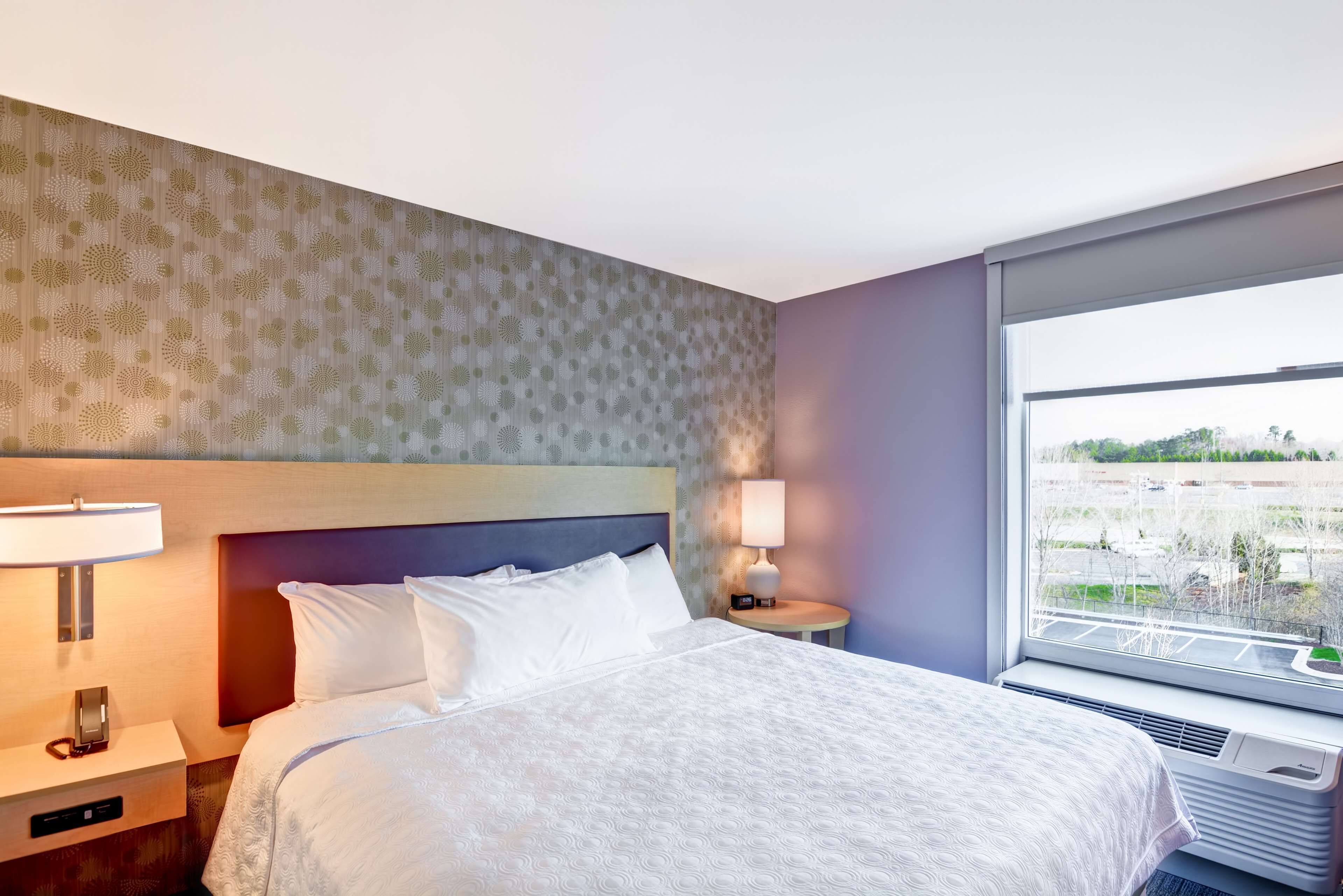 Habitación de hotel con cama, lámparas de noche, mesita de noche, ventana con vistas y pared con papel tapiz estampado.