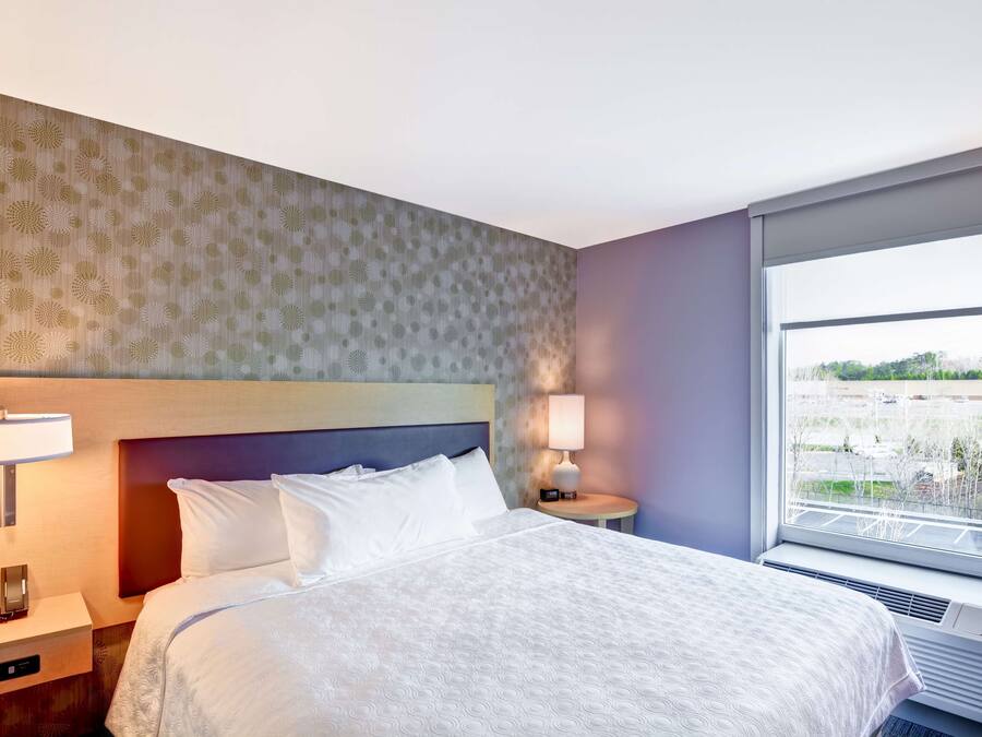 Habitación de hotel con cama, lámparas de noche, mesita de noche, ventana con vistas y pared con papel tapiz estampado.